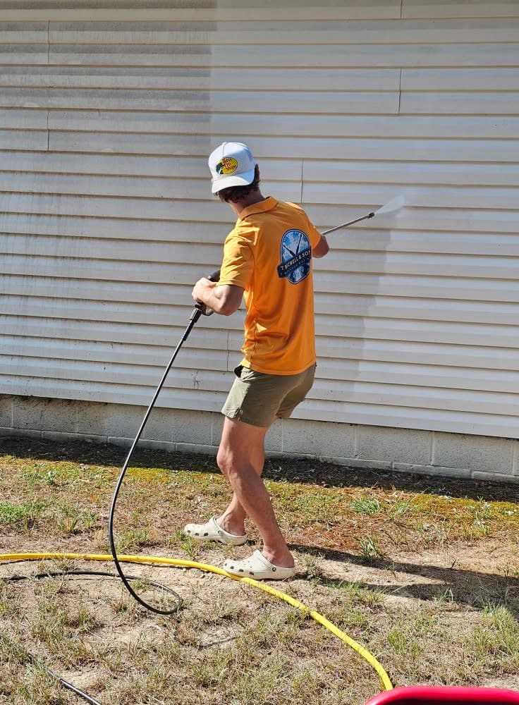 Trichell & Sons crew member in branded shirt pressure washing house siding